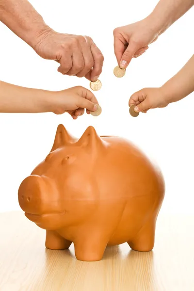Mãos de gerações diferentes colocando moedas no banco porquinho — Fotografia de Stock