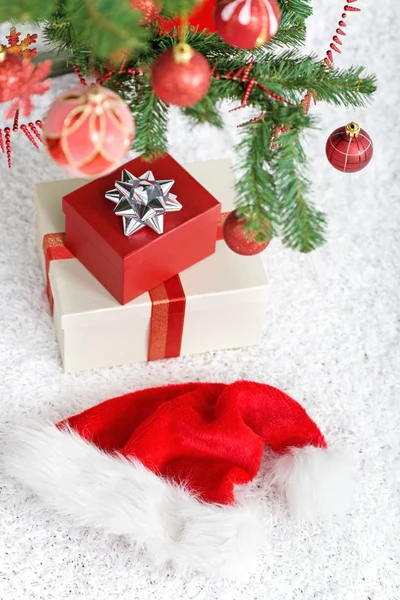 Presents and santa hat under the christmas tree — Stock Photo, Image