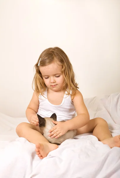 Klein meisje zitten in bed met haar kitten — Stockfoto