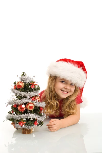 Niña sonriente asomándose a un pequeño árbol de Navidad —  Fotos de Stock