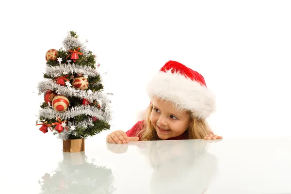 Happy kid lurking around a small christmas tree — Stock Photo, Image