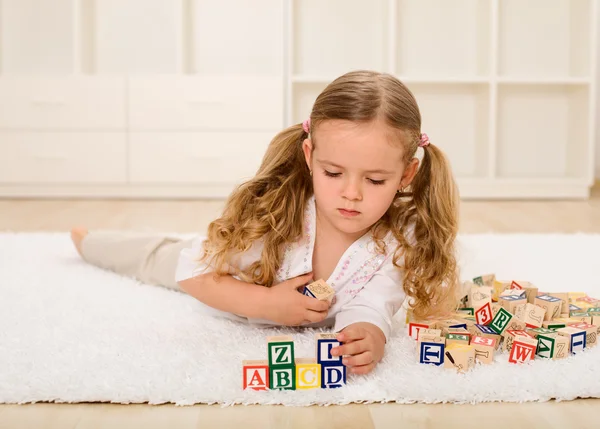 Маленька дівчинка грає з дерев'яними блоками на підлозі — стокове фото
