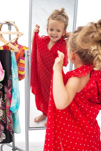 Glückliches kleines Mädchen probiert Kleider vor dem Spiegel an — Stockfoto