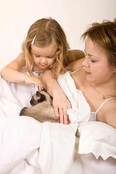 Dziewczynka i jej matka w łóżku z kotkiem — Zdjęcie stockowe