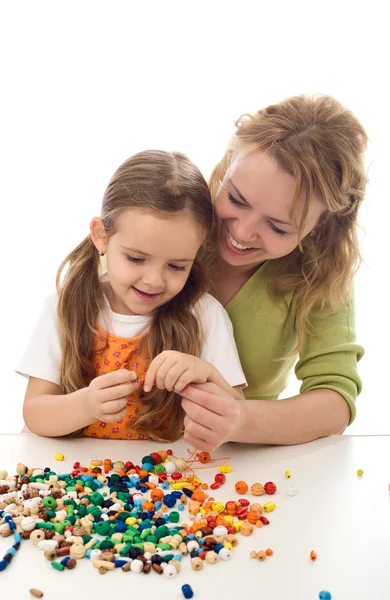 Kvinna och liten flicka leker med pärlor och en sträng — Stockfoto