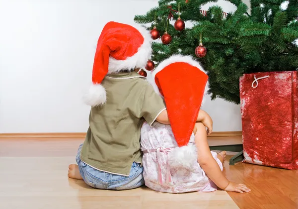 Crianças olhando para a árvore de Natal abraçando — Fotografia de Stock