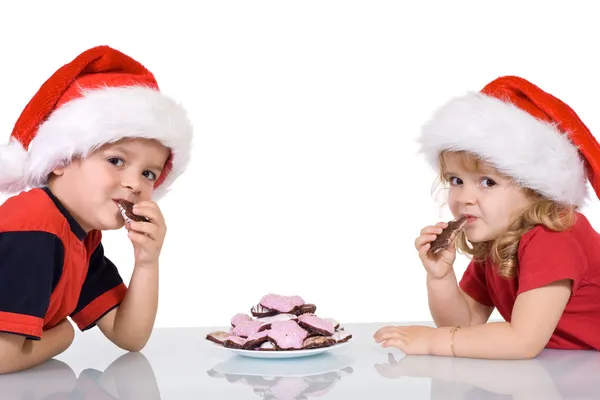 Crianças com chapéus de Papai Noel comer cookies — Fotografia de Stock