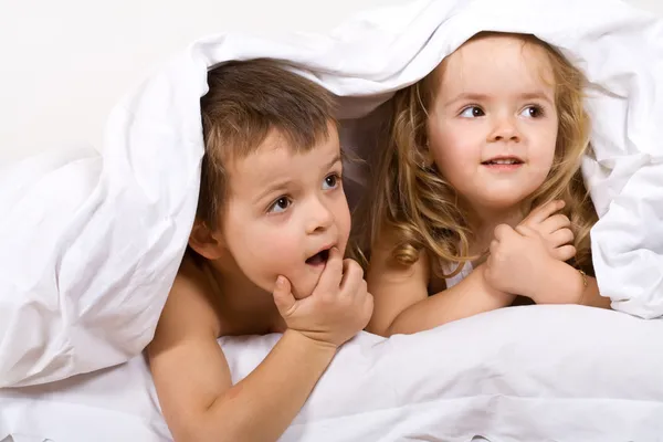 Crianças brincando debaixo da colcha na cama — Fotografia de Stock