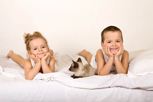Děti, kterým se v posteli s jejich kotě — Stock fotografie
