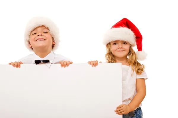Happy kids with santa hats and white cardboard — Stock Photo, Image