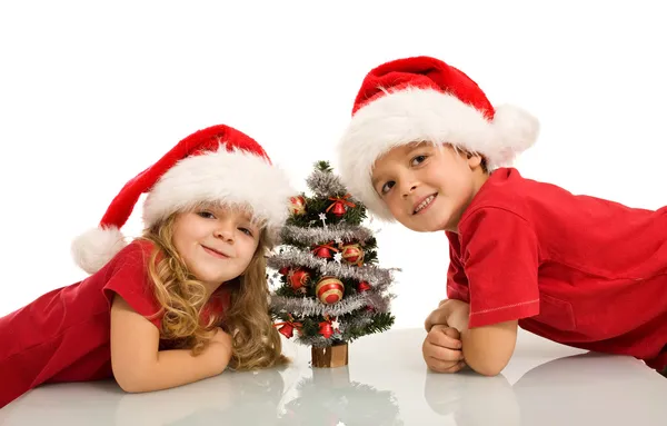 Glückliche Kinder mit Weihnachtsmützen und kleinem Weihnachtsbaum — Stockfoto