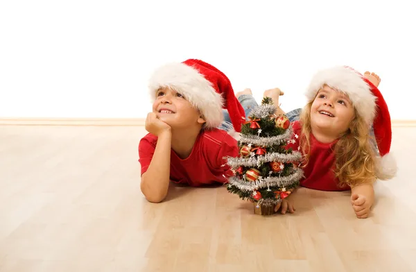 Niños felices con sombreros de Santa Claus tirados en el suelo —  Fotos de Stock