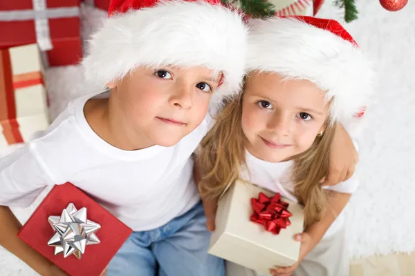 Weihnachtskinder mit Weihnachtsmützen und Geschenken — Stockfoto