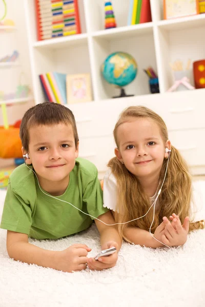 Kids sharing a music player laying on the floor — Stock Photo, Image