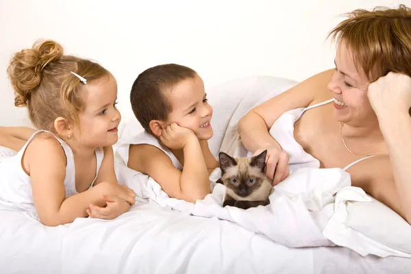 Mulher e crianças com um gatinho preguiçando na cama — Fotografia de Stock