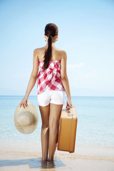 Young female standing on the beach with retro suitcase