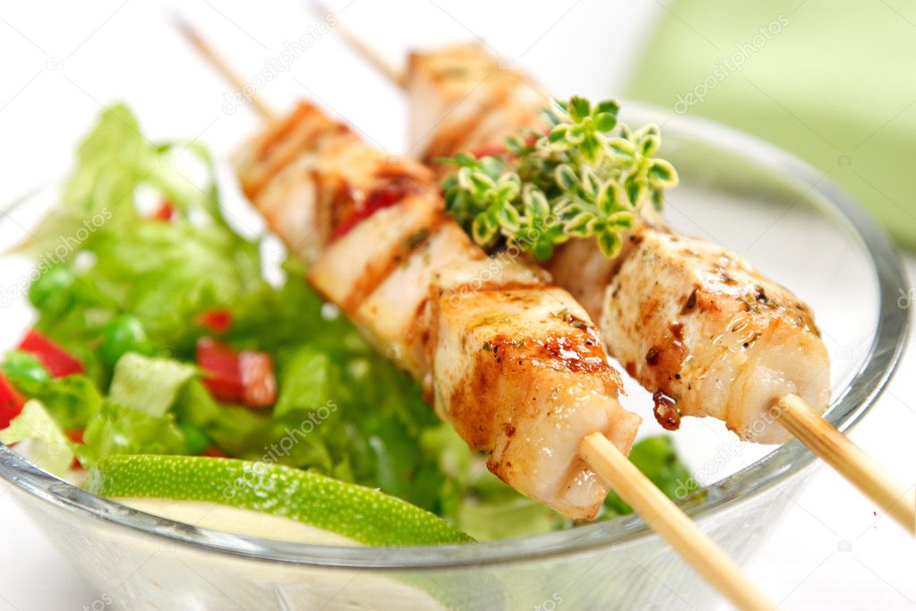Pork (or chicken) on a grill spit with salad and a slice of lime and lemon-