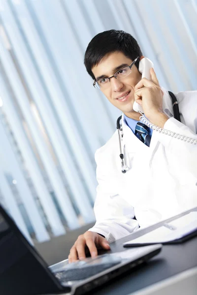 Médico de sucesso com telefone e laptop, no escritório — Fotografia de Stock