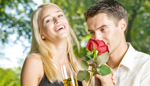 Jonge gelukkige paar met champagne, cadeau en rose, buitenshuis — Stockfoto
