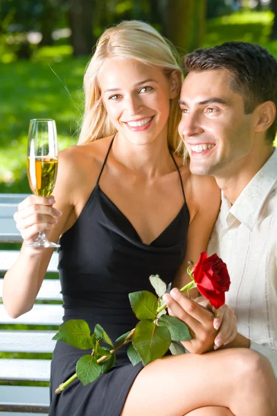 Giovane coppia felice con champagne, regalo e rosa, all'aperto — Foto Stock