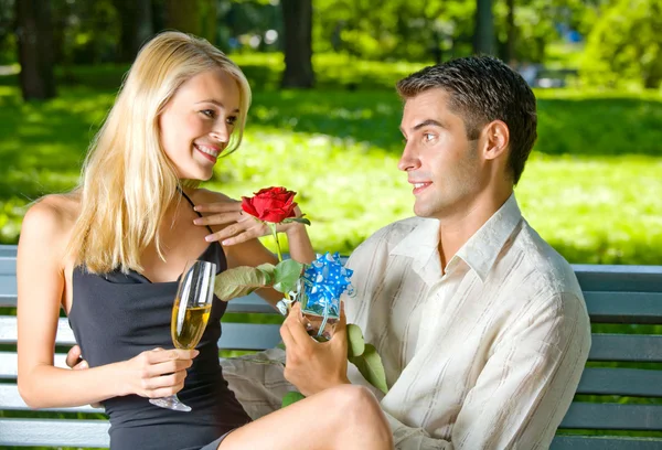 Engraçado jovem casal feliz com presente e rosa, ao ar livre — Fotografia de Stock
