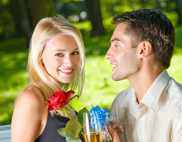 Junges glückliches Paar mit Champagner, Geschenk und Rose, im Freien — Stockfoto