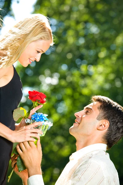 Giovane coppia felice con rosa e regalo, all'aperto — Foto Stock