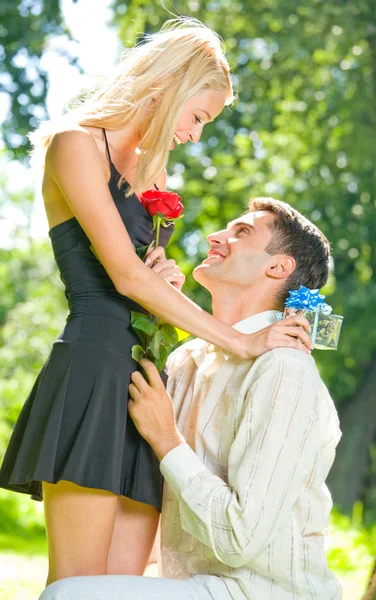 Lustiges junges glückliches Paar mit Geschenk und Rose, im Freien — Stockfoto