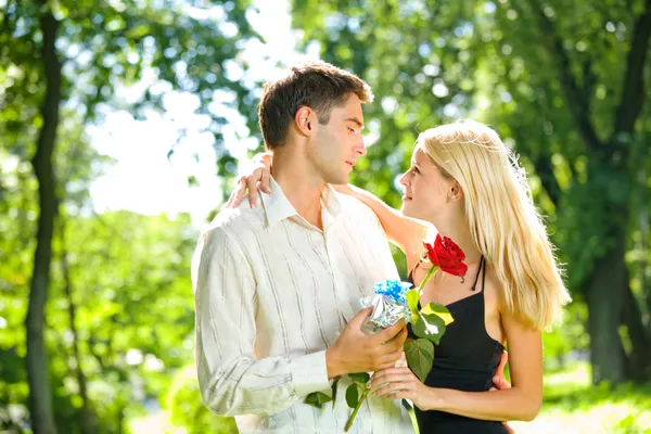 Jovem casal feliz com presente e rosa, ao ar livre — Fotografia de Stock