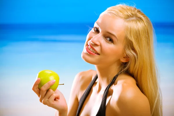 Unga vackra leende kvinna med apple på stranden — Stockfoto