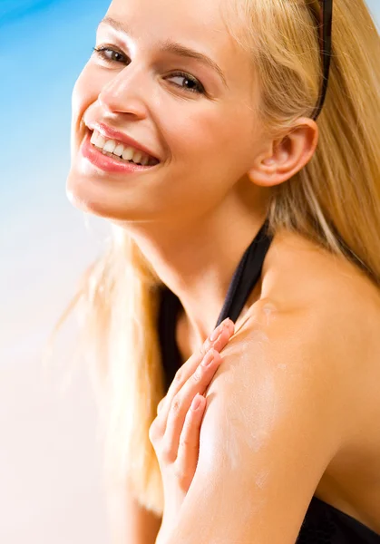 Νεαρή όμορφη χαμογελαστό γυναίκα με κρέμα προστασία από τον ήλιο στην παραλία — Φωτογραφία Αρχείου