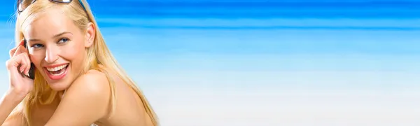年轻漂亮的金发碧眼女人用在海滩上的手机。到上一页 — 图库照片