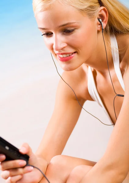 Giovane donna sorridente con cellulare o lettore multimediale sulla spiaggia — Foto Stock
