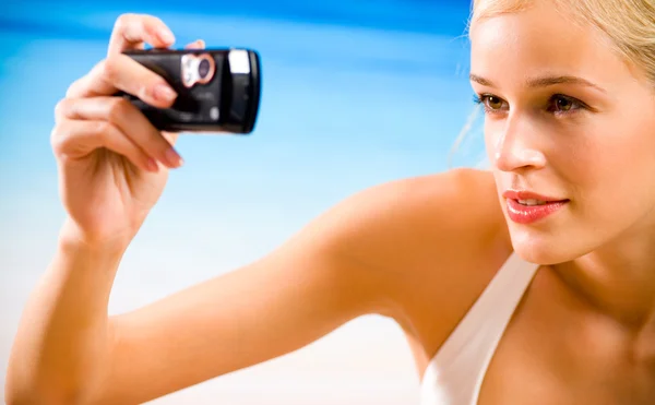 Молодая женщина фотографирует по мобильному телефону на морском пляже — стоковое фото