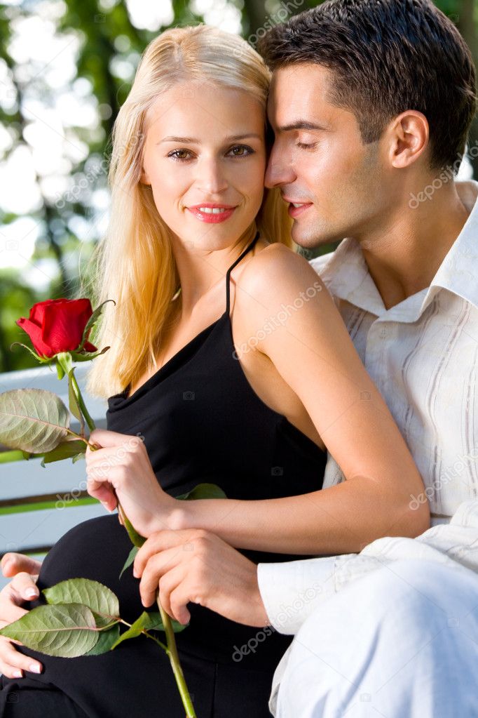 Happy Pregnant Woman With Rose And Her Husband Outdoors