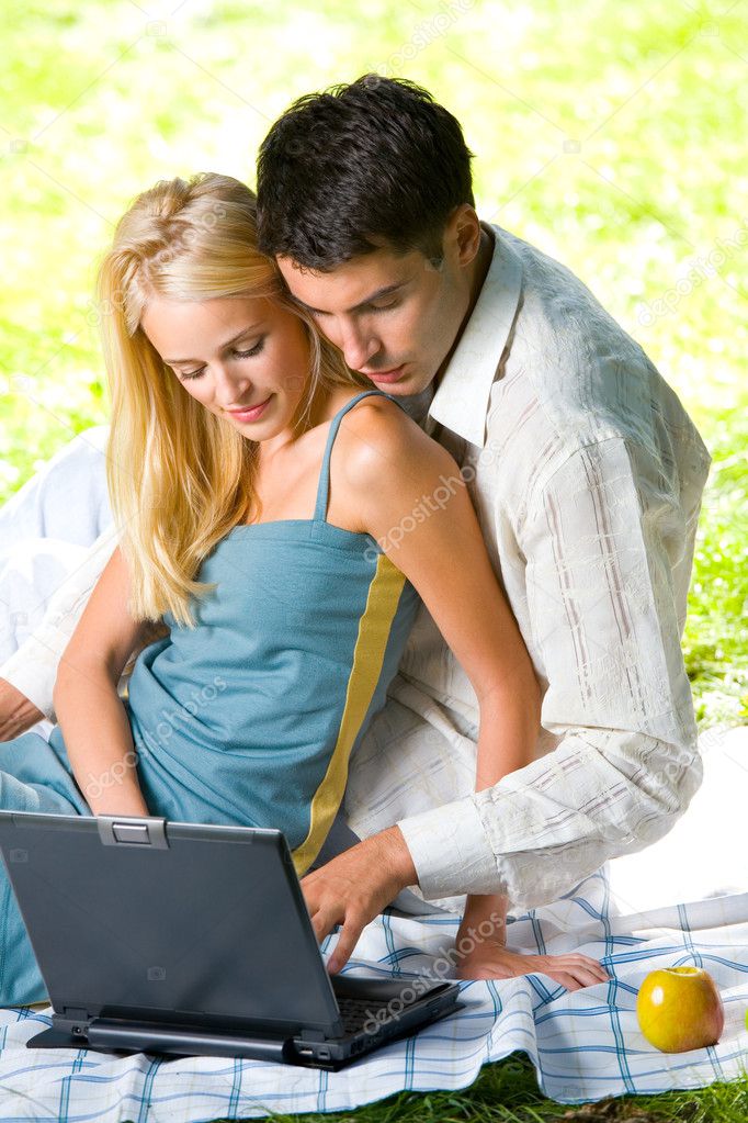 Young happy smiling couple with laptop at picnic