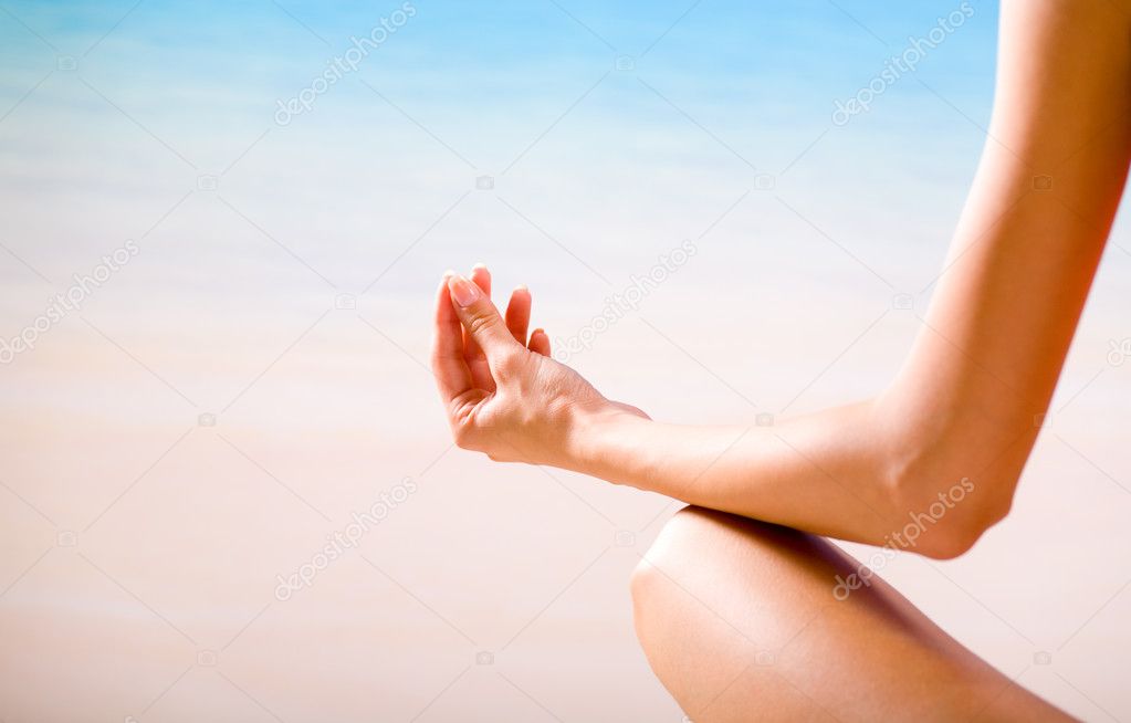 Young woman doing yoga moves or meditating on tropical ocean bea