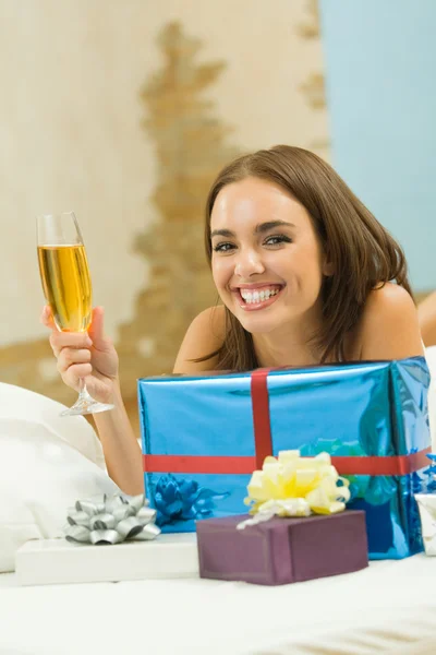 Νεαρή χαρούμενη χαμογελαστή γυναίκα με δώρα και σαμπάνια στο σπίτι — Φωτογραφία Αρχείου