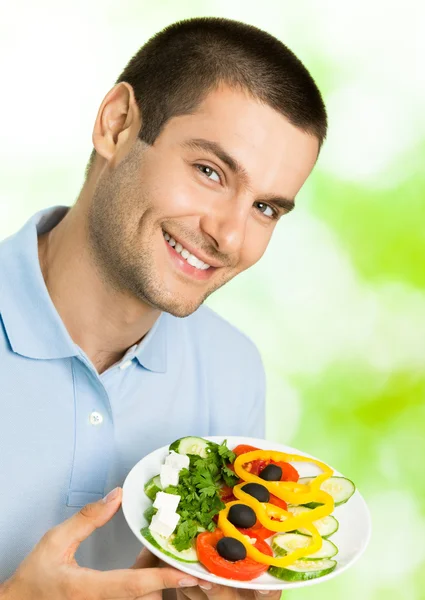 Портрет молодого счастливого улыбающегося человека с тарелкой салата, на открытом воздухе — стоковое фото