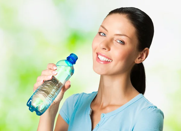 Молодая улыбающаяся женщина с бутылкой воды, на открытом воздухе — стоковое фото