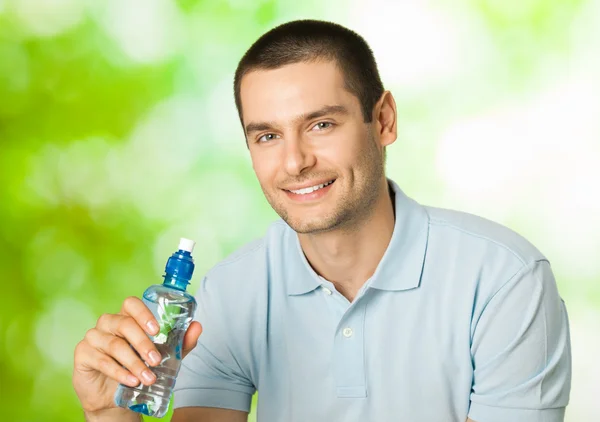 Jonge gelukkig lachende man met fles water, buitenshuis — Stockfoto