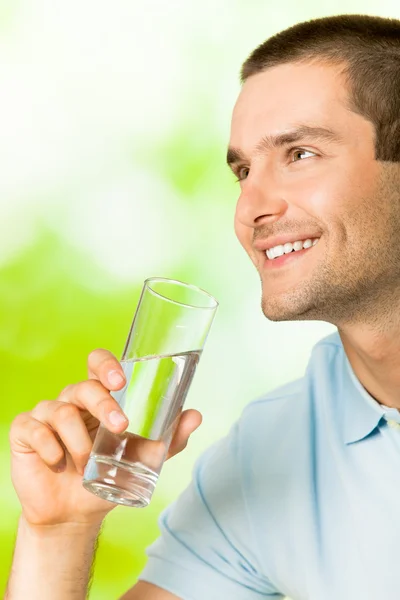 Giovane uomo sorridente con un bicchiere d'acqua, all'aperto — Foto Stock