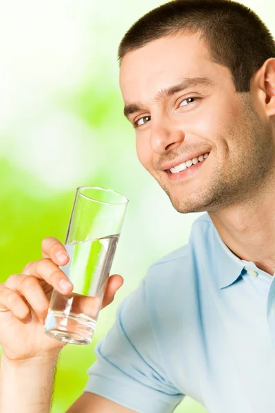 Молодой улыбающийся мужчина со стеклом воды, на открытом воздухе — стоковое фото