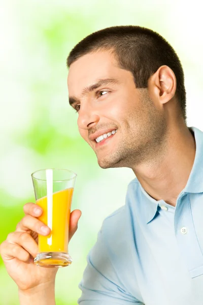 Giovane uomo sorridente con succo d'arancia, all'aperto — Foto Stock