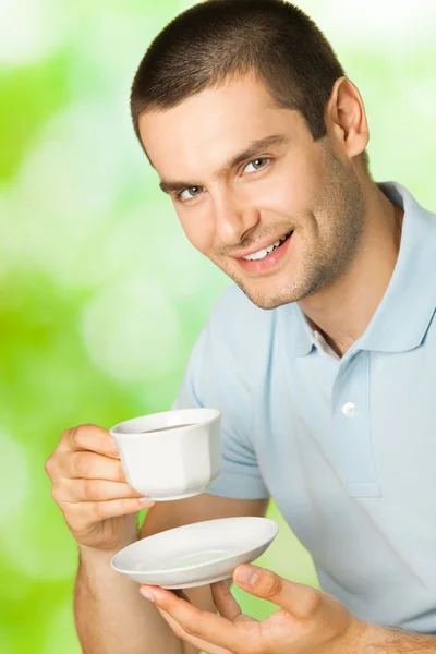 Portret młodego człowieka uśmiechający się zadowolony, picia kawy, na zewnątrz — Zdjęcie stockowe