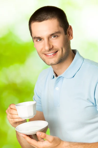 Молодой счастливый улыбающийся мужчина пьет кофе на открытом воздухе — стоковое фото