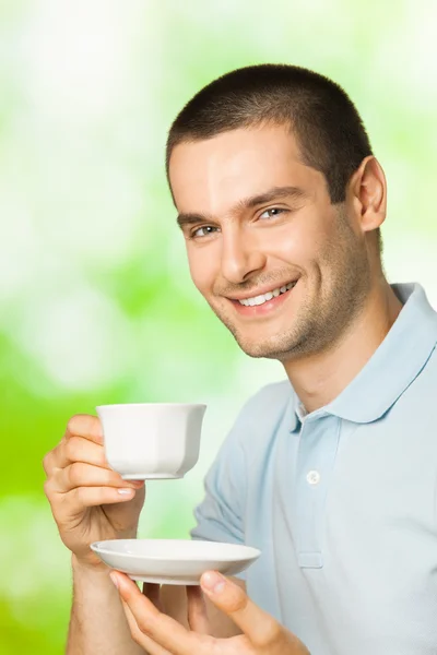 Портрет молодого счастливого улыбающегося мужчины, пьющего кофе на открытом воздухе — стоковое фото