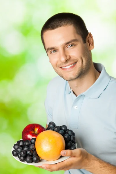 Portrait de jeune homme souriant heureux avec assiette de fruits, outdoo — Photo