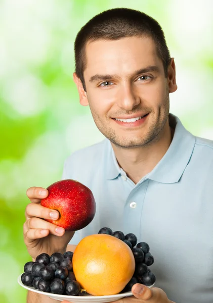 Retrato de joven feliz hombre sonriente con plato de frutas, outdoo —  Fotos de Stock