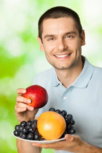 Porträtt av ung glada leende man med platta med frukter, utomhu — Stockfoto
